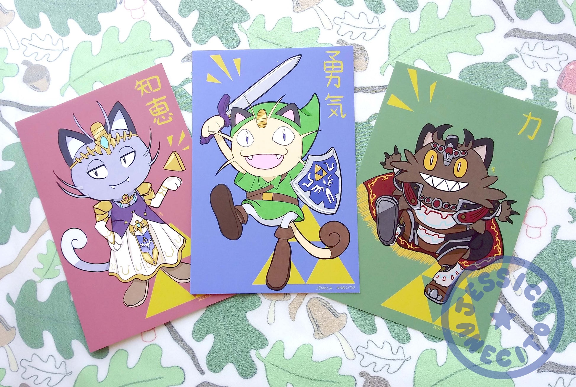 All three available designs of postcard are spread out together on a surface covered in a forest printed cloth. The leftmost print is alolan version Meowth, dressed as Princess Zelda. The middle print is the original design for Meowth, dressed as Link and the rightmost design is the Galarian form of Meowth, dressed as Ganon